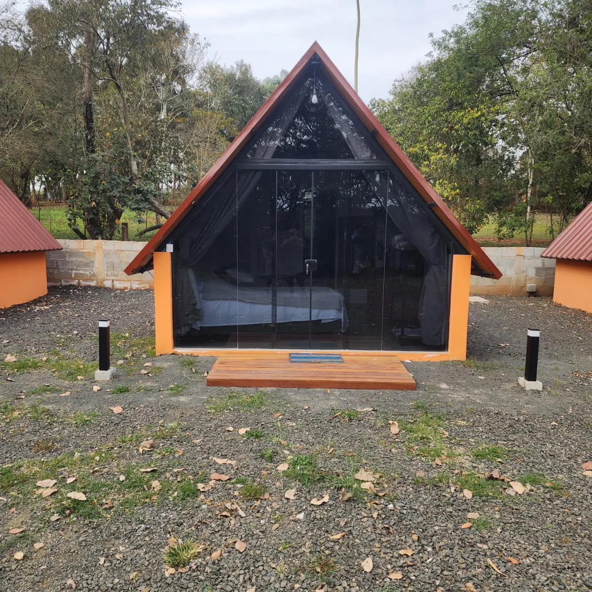 Fachada frontal de um chalezinho com parede de vidro e deck de madeira