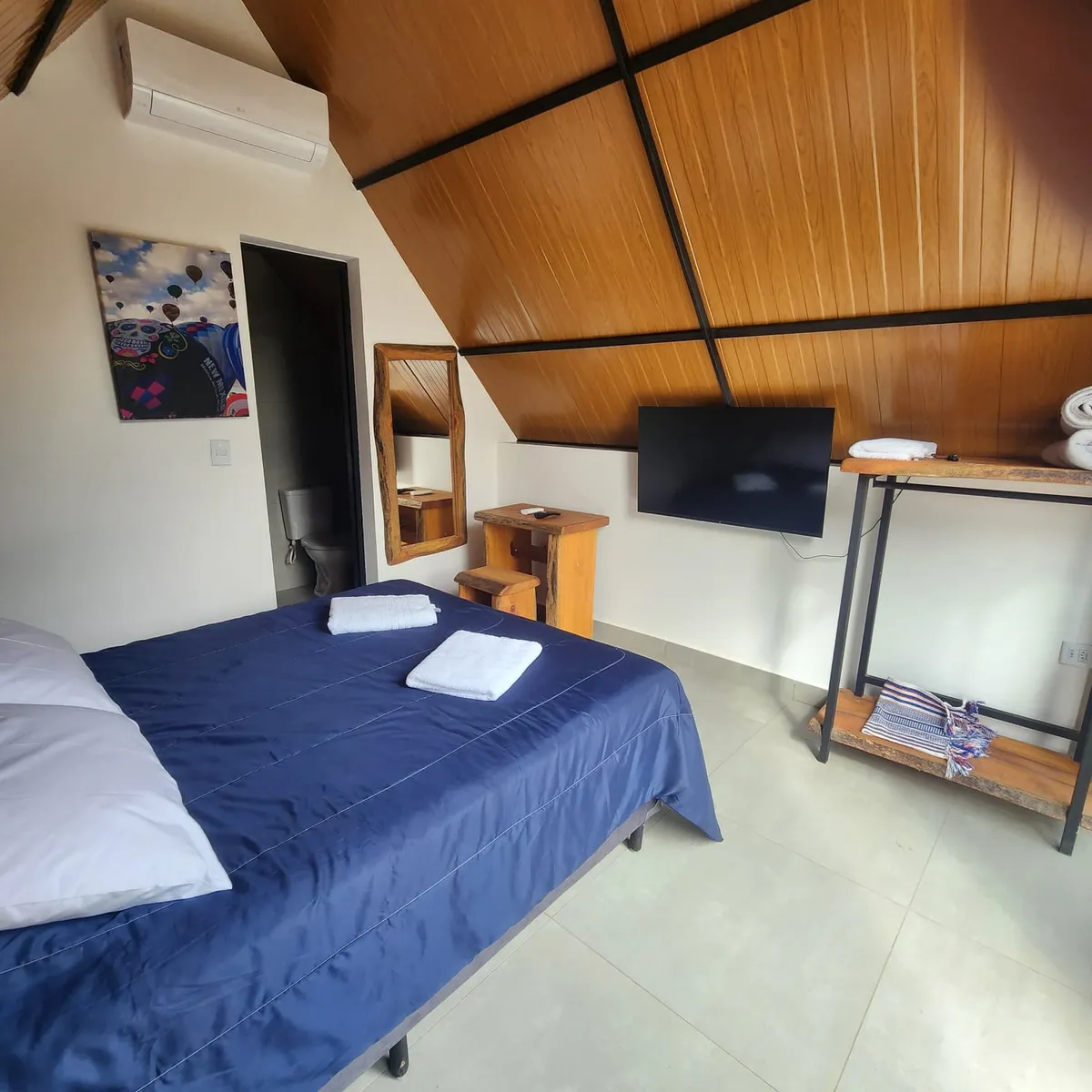 Interior do chalezinho — cama de casal, TV e ar-condicionado
