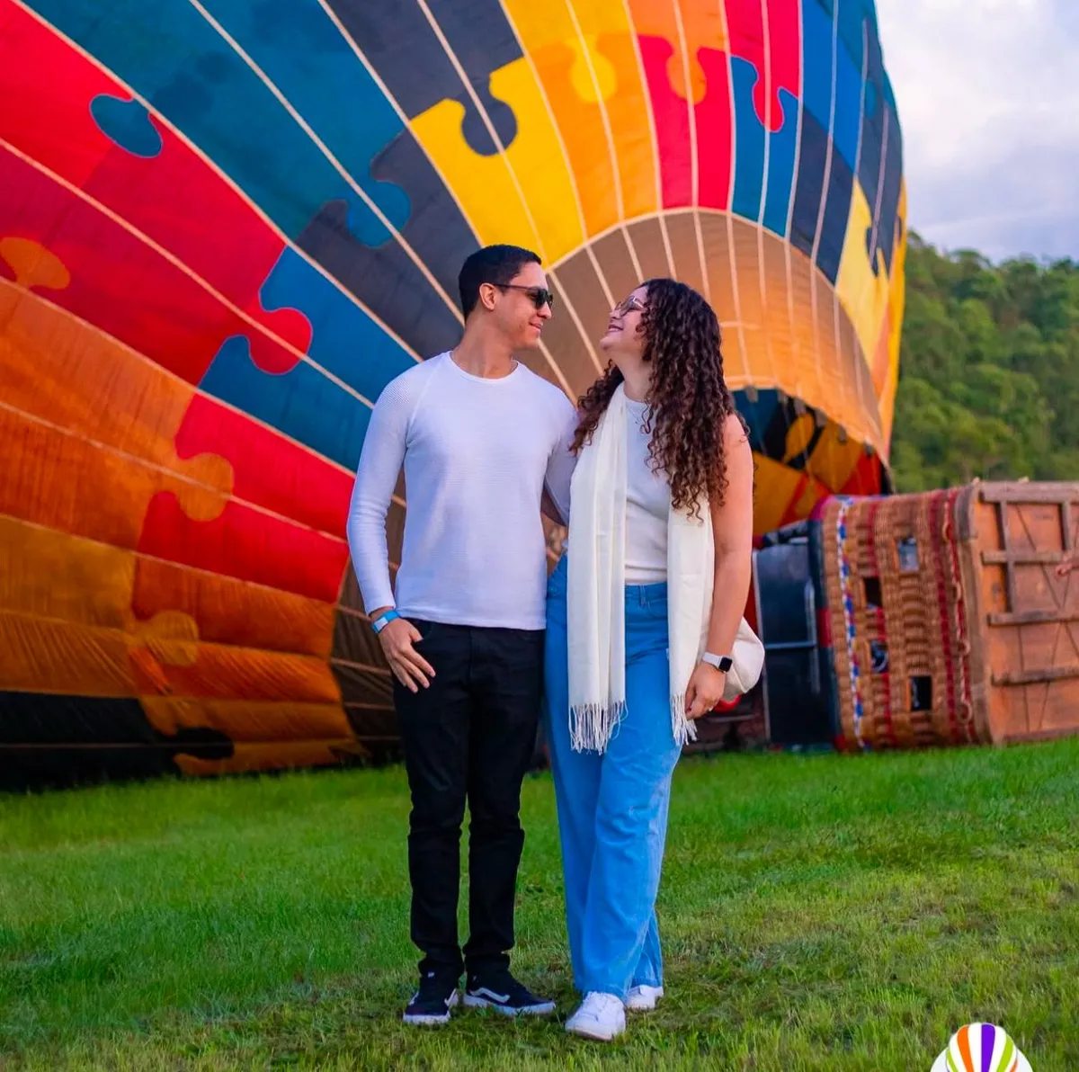 Casal sorrindo em frente a balão colorido no campo de decolagem